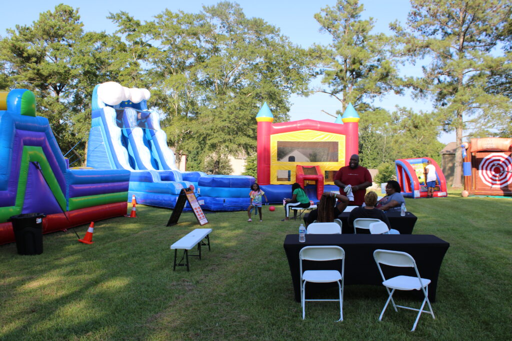 Families enjoying multiple bounce houses, water slides, and inflatable games at an outdoor event in Douglasville, Georgia hosted by Marques Amusement Company