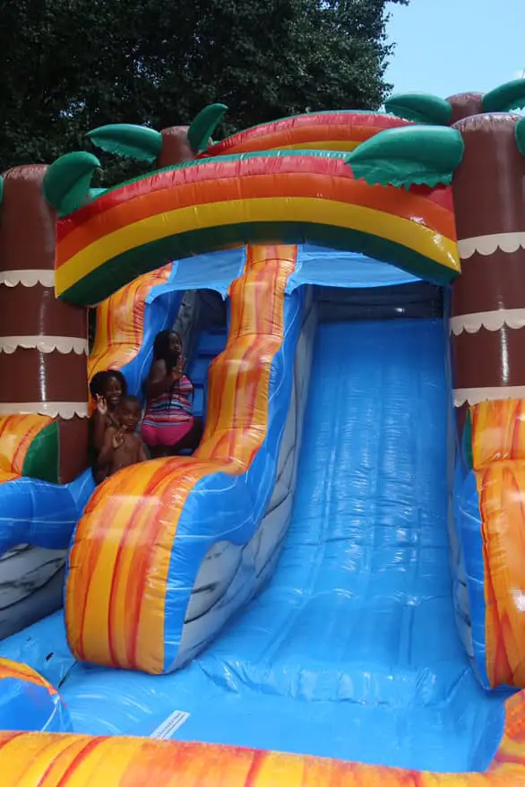 Children sliding down a tropical-themed inflatable water slide at an outdoor party in Atlanta, Georgia